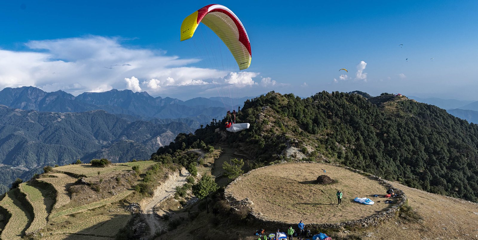 A paraglider airborne over the green terraced ridges at Bir Billing