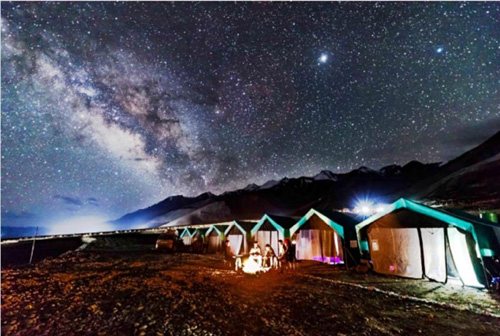 Lit camp tents beside a Ladakhi lake beneath the Milky Way